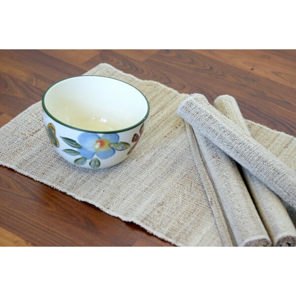 Beige woven placemats stacked beside a floral patterned ceramic bowl on a wooden table in soft natural light